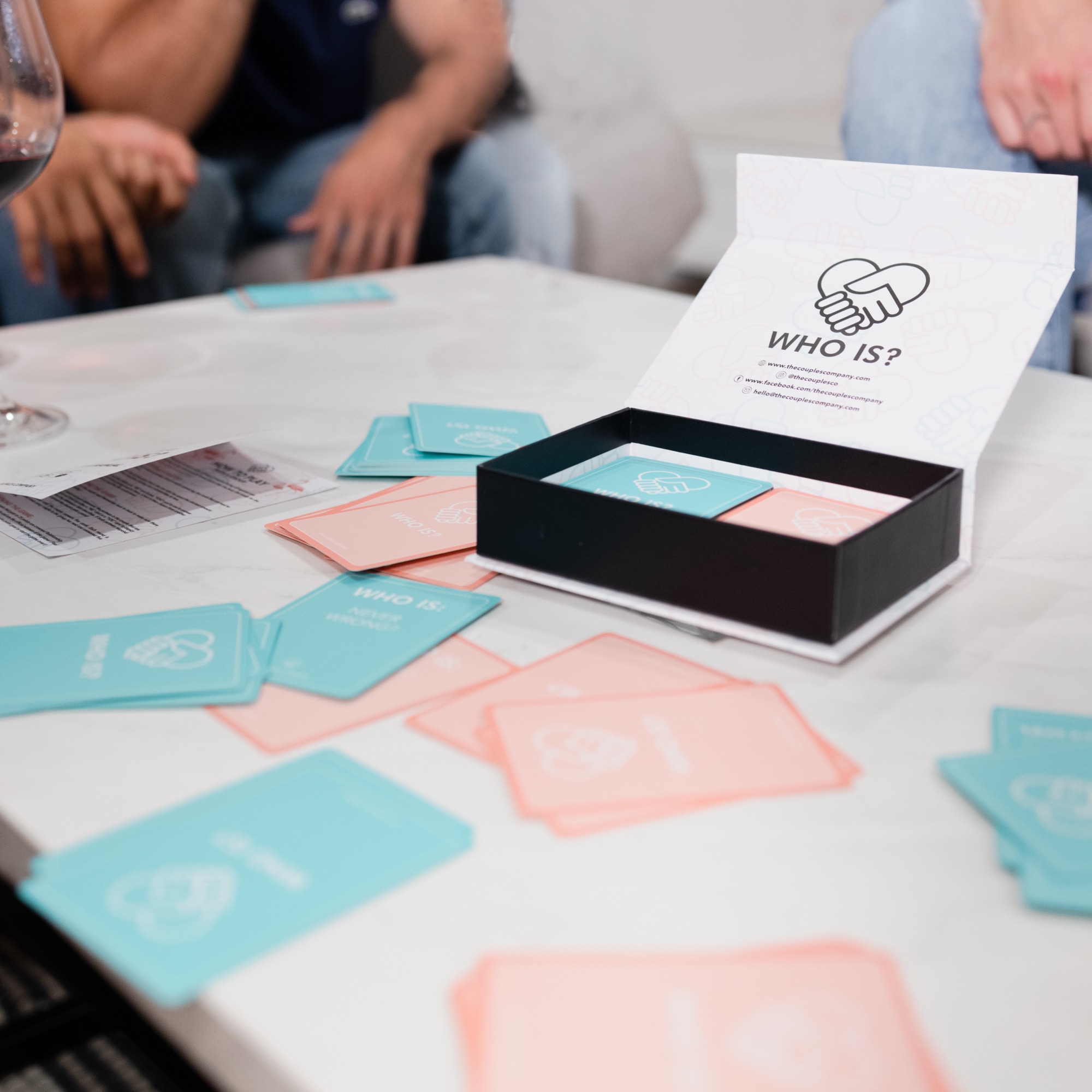 The open WhoIs? box with pink and teal cards fanned out on marble